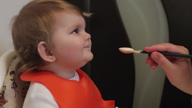 Baby girl in high chair mischievously teases mom holding spoonful of food