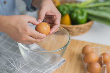 Young woman cooking in a bright kitchen, hand made cracked fresh egg yolks dripping into the bowl. Preparing ingredients for healthy cooking. Homemade food