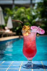 tropical singapore sling cocktail in tall glass by swimming pool - 606704342