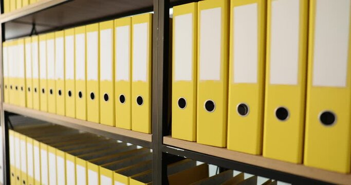 Yellow folders structure with materials on shelves of rack in company office. Room for archives and storage of documents in ring binders. Concept of saving data