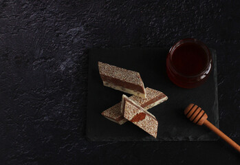 milk-chocolate halva with sesame seeds and nuts in pieces on a board on a dark background