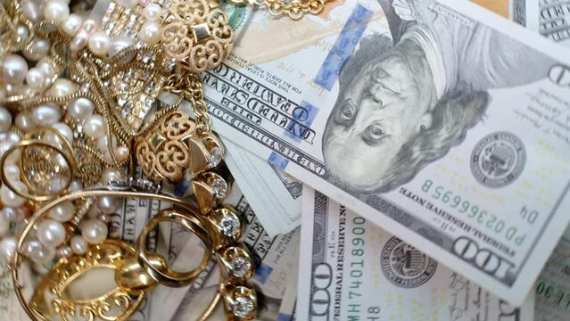 4k rotating footage top view of many one hundred dollar bills and gold jewelry.US currency, precious metals and stones. Profit. Accumulated values. Vintage expensive rare things. Diamonds, pearls.