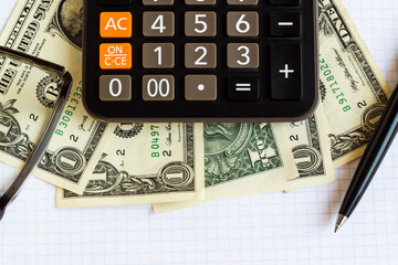 One US Dollar Bills on white checkered paper with calculator,pen and glasses.Conceptual image of finance
