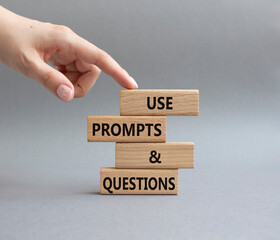 Prompts and Questions symbol. Concept word. Use Prompts and Questions on wooden blocks. Beautiful grey background. Businessman hand. Business and Prompts and Questions concept. Copy space