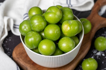 Green plum in bowl. Organic farm products. Sweet or sour plum on a dark background. Close up