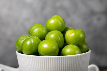 Green plum in bowl. Organic farm products. Sweet or sour plum on a dark background. Close up