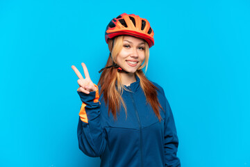 Young cyclist girl isolated on blue background smiling and showing victory sign