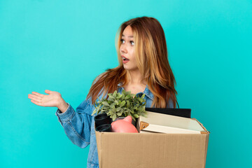 Teenager blonde girl making a move while picking up a box full of things with surprise expression...