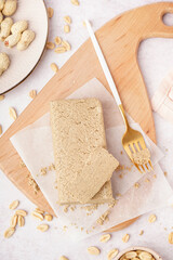 Board with tasty halva and peanuts on white background