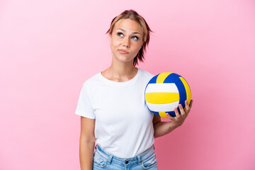 Young Russian woman playing volleyball isolated on pink background and looking up