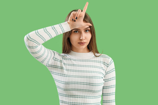 Young woman showing loser gesture on green background