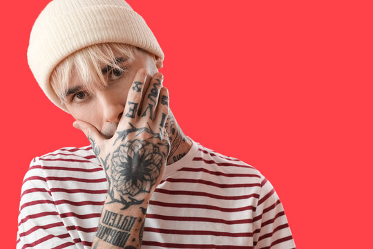 Tattooed young man in hat on red background, closeup