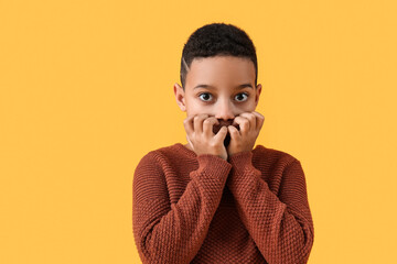 Scared little African-American boy on yellow background