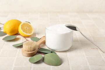 Bowl of baking soda, cleaning brush, lemons and eucalyptus branch on light tile table