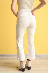 Young woman in white jeans near yellow wall, back view