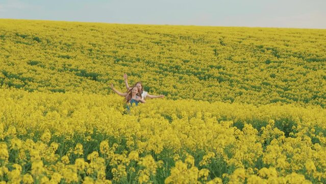 two joyful happy little girls run through blooming rapeseed field of yellow flowers. Joyful cheerful kids smiling face play catch up enjoy summer nature. Blue spring sky sun light. Joy teens lifestyle