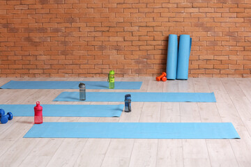 Fototapeta Yoga mats with bottles of water near brick wall in gym obraz