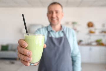 Mature man with glass of fresh vegetable smoothie in kitchen, closeup