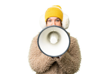 Young girl wearing winter muffs over isolated chroma key background shouting through a megaphone