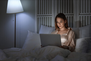 Young woman using laptop in bedroom at night