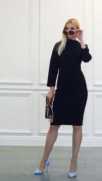 Serious businesswoman in sunglasses and tight black dress with handbag