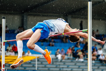 close-up man athlete high jump in rain, summer athletics championships, fosbury flop technique