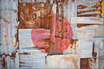 Flag of Japan on rusty corrugated iron sheets forming a wall or a fence