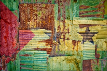 Flag of Sao Tome painted onto rusty corrugated iron sheets overlapping to form a wall or fence
