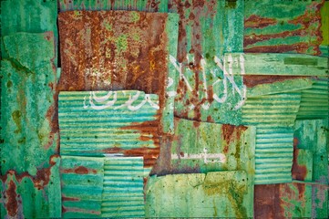 Flag of Saudi Arabia painted onto rusty corrugated iron sheets overlapping to form a wall or fence