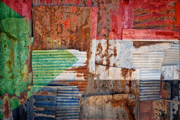 Flag of Sudan painted onto rusty corrugated iron sheets overlapping to form a wall or fence