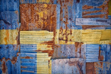 Flag of Sweden painted onto rusty corrugated iron sheets overlapping to form a wall or fence