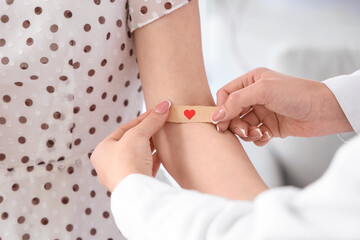 Female doctor applying medical patch on young donor's arm in clinic, closeup