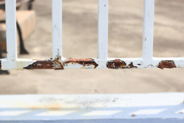 Rust that has formed on the iron fence is causing the paint to peel off, the fence is rusty.