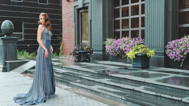  young sexy woman fashion model stands posing. Beautiful girl, long red hair, elegant hairstyle wave retro style. Gray blue festive prom evening dress. city street cityscape. Luxury trendy lady bride