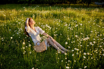 a beautiful woman in a light dress sits in a field in chamomile flowers.