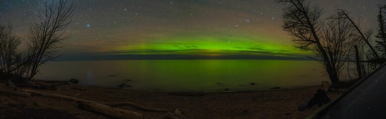 Panoramic view of a starry sky with the green glow of the northern lights over a serene lake