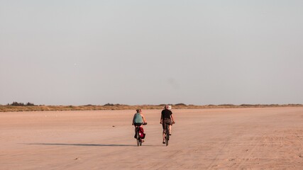 Fototapeta na wymiar Women riding bicycles on the sandy shore of Fano Island on a sunny day. Denmark