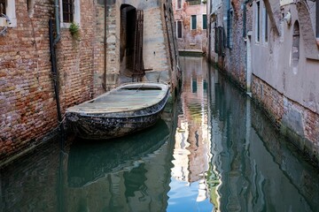 Old boat floating on a canal through historic buildings in Venice, Italy