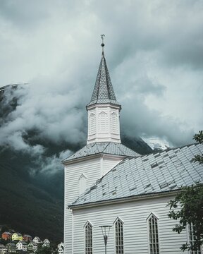 Vertical of the white Hyen church in Norway with a mountain hiding behind a cloud in the background