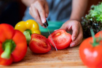 girl cook in the kitchen cuts a tomato with vegetables with a knife