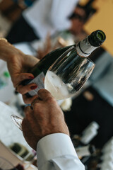 White wine poured into a glass by a waiter at a tasting in a restaurant. - 606766368