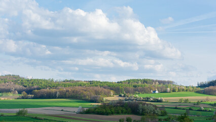 pola i lasy na pagórkowatym terenie, białe obłoki chmury na błękitnym niebie