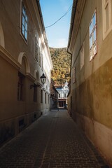 Obraz premium Narrow alley with stone floor between buildings with mountains trees in Brasov, Romania