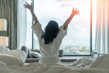 Hotel relaxation on lazy day with Asian woman waking up from good sleep on bed in weekend morning resting in comfort bedroom celebrating having happy work-life quality balance lifestyle - obrazy, fototapety, plakaty