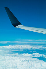 白い雲と青い空、飛ぶ飛行機の翼。