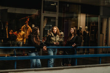 Front view shot of three lovely girls leaning on a blue fence at the shopping mall while discussing fashion and prices
