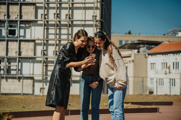 Three lovely girls looking at the phone. Brunette girl (left) showing the pictures to her friends that she took of them