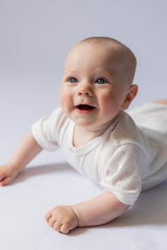 portrait of a cute baby 5 months old in a white bodysuit on a white background in the studio, smiling looking into the frame. Baby's health, newborn baby, space for text