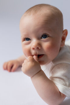 portrait of a cute baby 5 months old in a white bodysuit on a white background in the studio, smiling looking into the frame. Baby's health, newborn baby, space for text