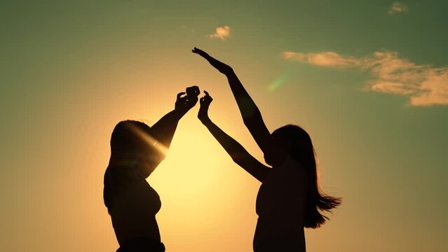 Friends have fun at beach party during sunset. Free girls dance merrily on summer evening, sun. Group of young people having fun dancing with raised hands to music. Celebrate summer day at beach party